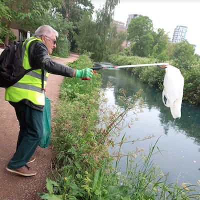 Someone picking a plastic bag out of a river using a stick