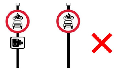 Two red, circular 'No motor vehicles' signs. One has a sign with a picture of a camera underneath. There's a red cross next to the signs. 