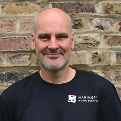 Man standing in front of brick wall wearing Haringey Music Service t-shirt.