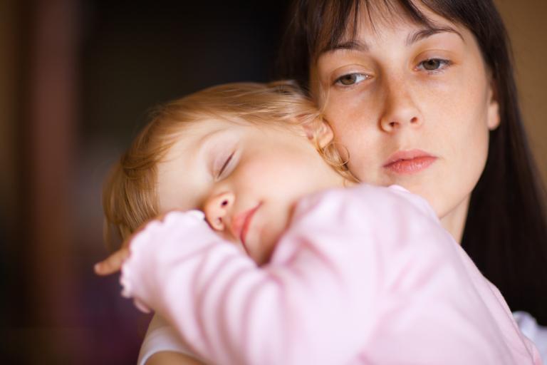 A child asleep with their head resting on their mother's shoulder.