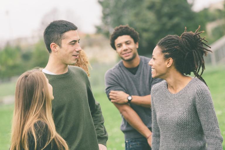 Diverse group of young people in a park talking and smiling