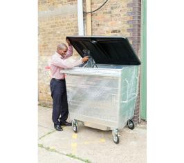 Man putting a black waste sack in a large silver wheelie bin with a black lid.