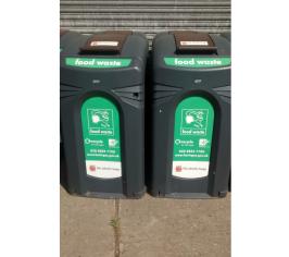 2 large black food waste bins side by side. With brown lids and green stickers with white writing.